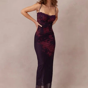 A woman in a fitted, floor-length purple dress with red floral detailing, thin straps, and sheer accents at the hem, posing against a neutral background.